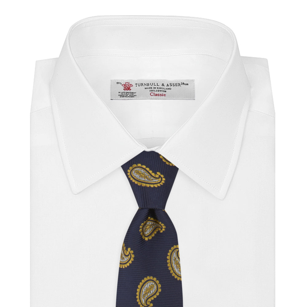 The Turnbull & Asser Navy and Gold Floating Paisley Silk Tie features a repeating yellow and white paisley pattern, shown rolled with the pointed end facing forward against a white background.
