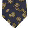 View 4 of product The Turnbull & Asser Navy and Gold Floating Paisley Silk Tie features a repeating yellow and white paisley pattern, shown rolled with the pointed end facing forward against a white background.