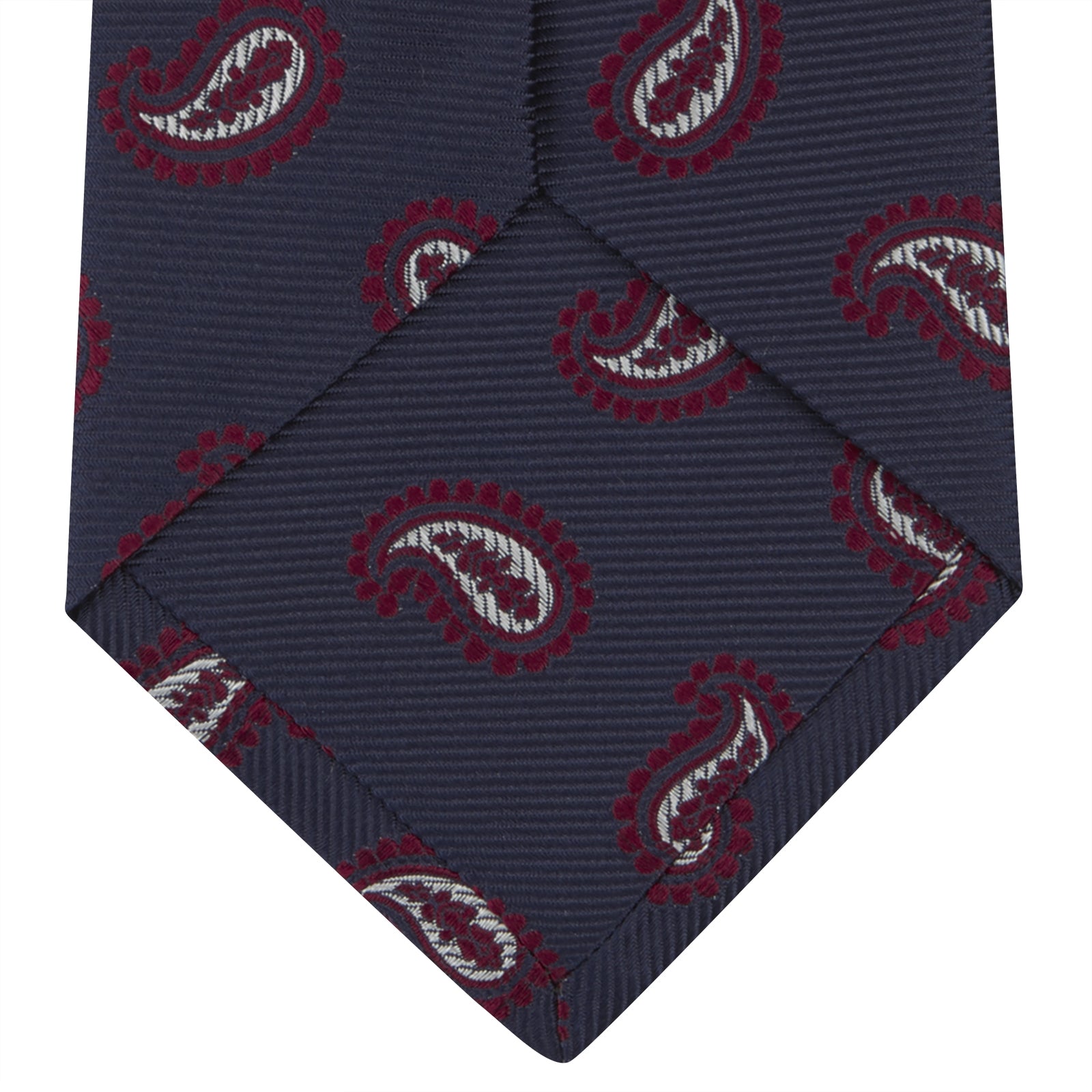 View 4 of product The Turnbull & Asser Navy and Burgundy Floating Paisley Silk Tie is shown rolled up, displaying its repeating paisley design on a plain white background.