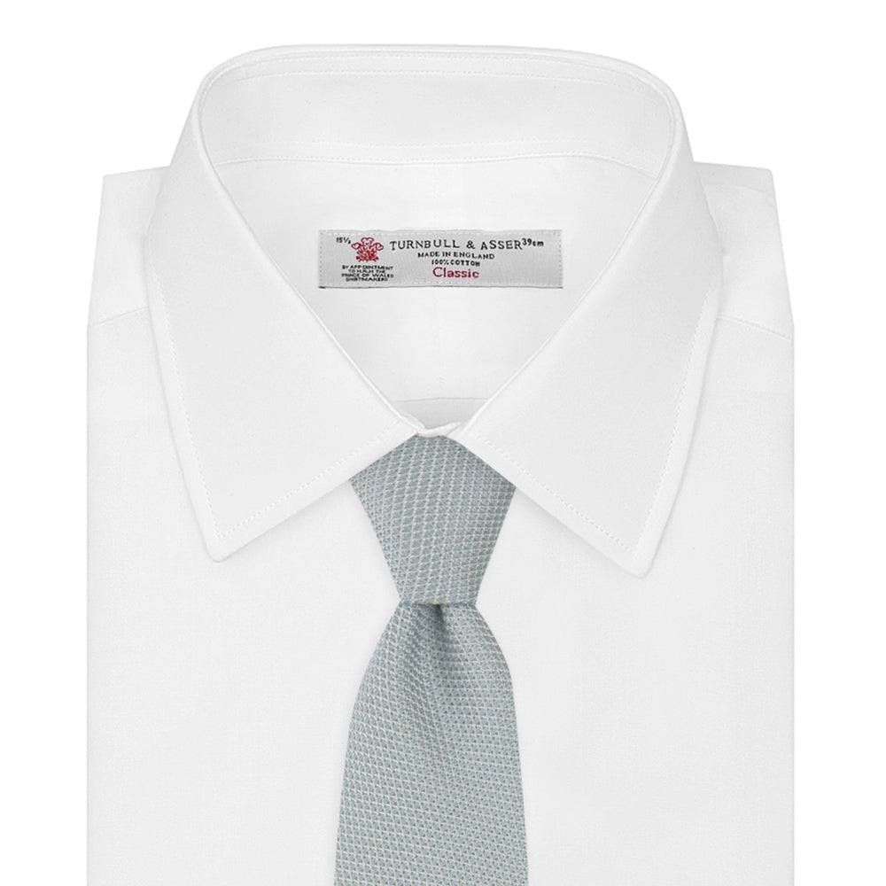 A neatly rolled Turnbull & Asser Light Blue Grenadine Silk Tie, featuring a subtle textured weave, displayed on a white background.