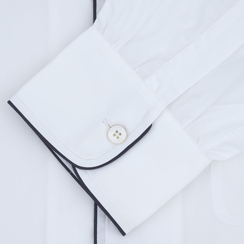 The Turnbull & Asser White Sea Island Quality Cotton Nightshirt, featuring black piping on the collar and pocket, is elegantly displayed folded against a light grey background.