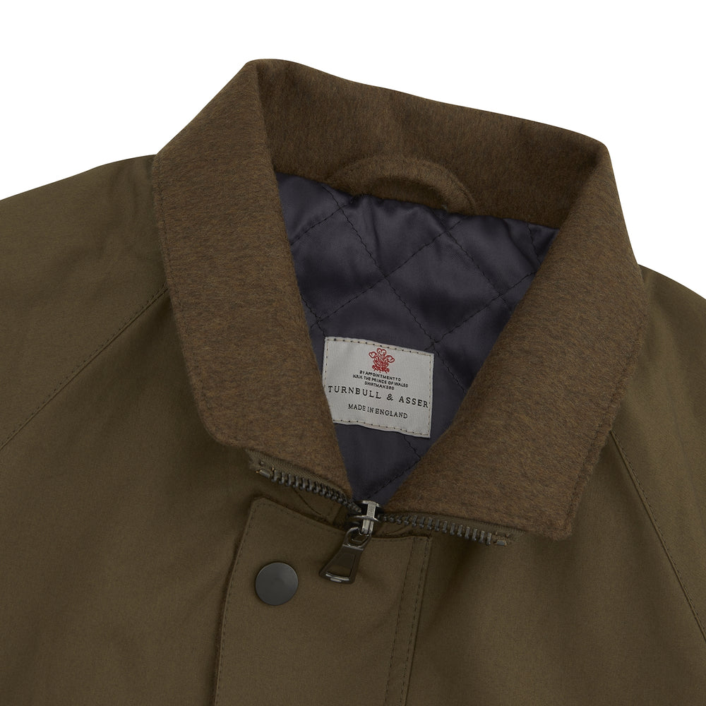 The Turnbull & Asser Dark Green Dry Wax Cotton Field Coat features a front zipper, snap buttons, two large flap pockets, two chest slant pockets, a stand collar, and a classic tailored design in durable dry wax cotton.