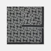 View 1 of product The Monochrome Paisley Mill Silk Pocket Square by Turnbull & Asser is a limited edition black silk accessory with a white paisley and floral pattern. The brand name appears in white text on the slightly folded bottom right corner.