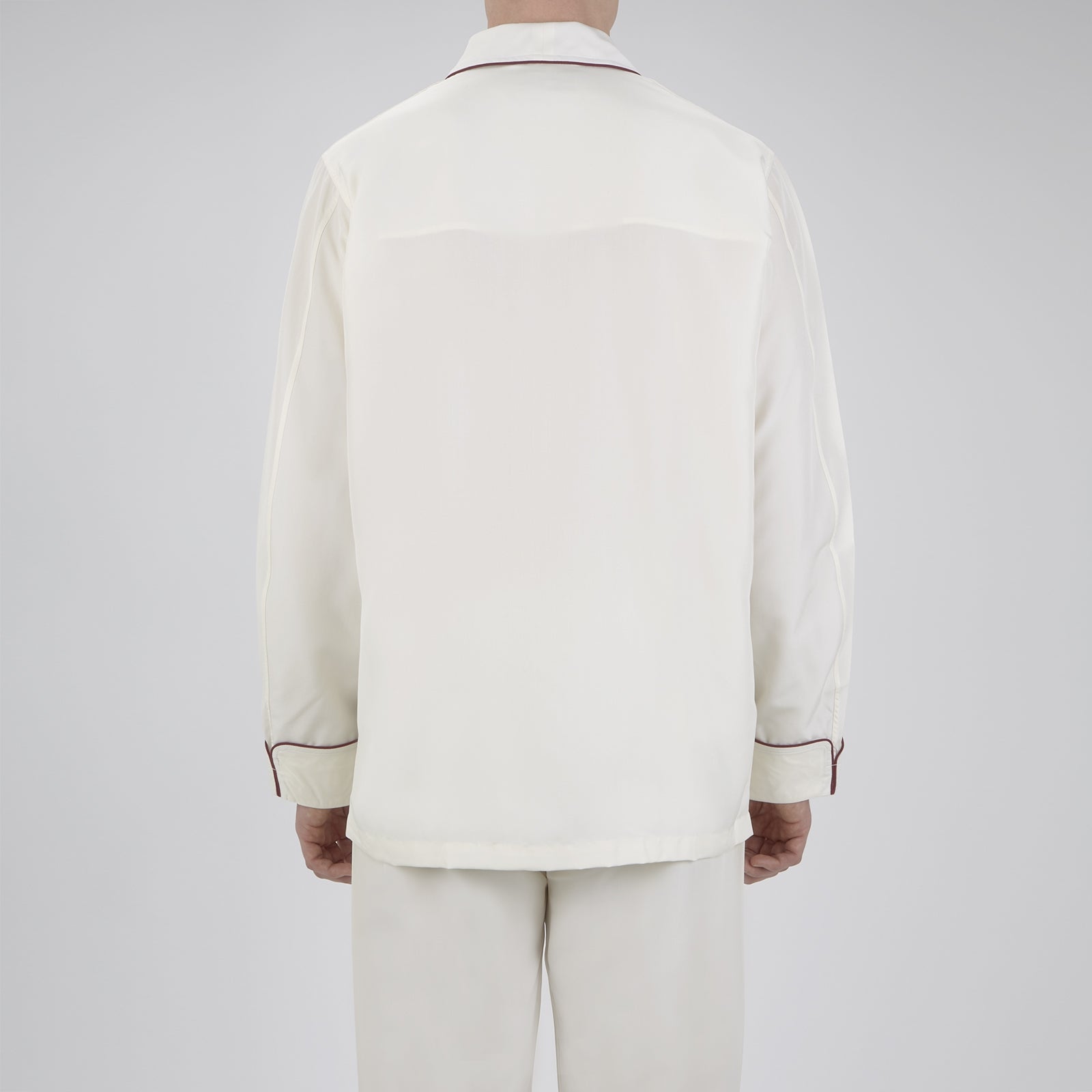 View 2 of product The Turnbull & Asser Cream Piped Silk Pyjama Set is neatly folded with dark piping and buttons, placed next to a matching white sleep mask with tie straps, all set against a light neutral background.