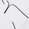 View 4 of product The Turnbull & Asser White Piped Cotton Pyjama Set, made from Egyptian cotton and featuring black piping and two buttons, is shown folded with a matching white tie-strap face mask on a light gray background.