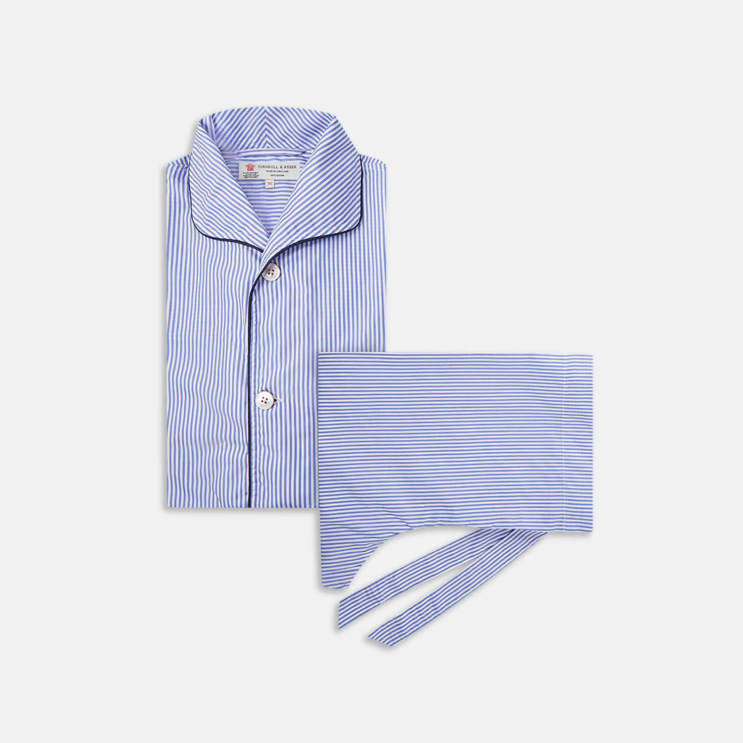 View 1 of product The Turnbull & Asser Blue Bengal Stripe Piped Cotton Pyjama Set, featuring a folded top with white buttons beside matching bottoms, is displayed on a plain light background.