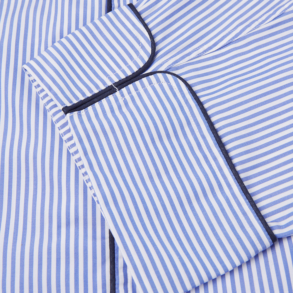The Turnbull & Asser Blue Bengal Stripe Piped Cotton Pyjama Set, featuring a folded top with white buttons beside matching bottoms, is displayed on a plain light background.