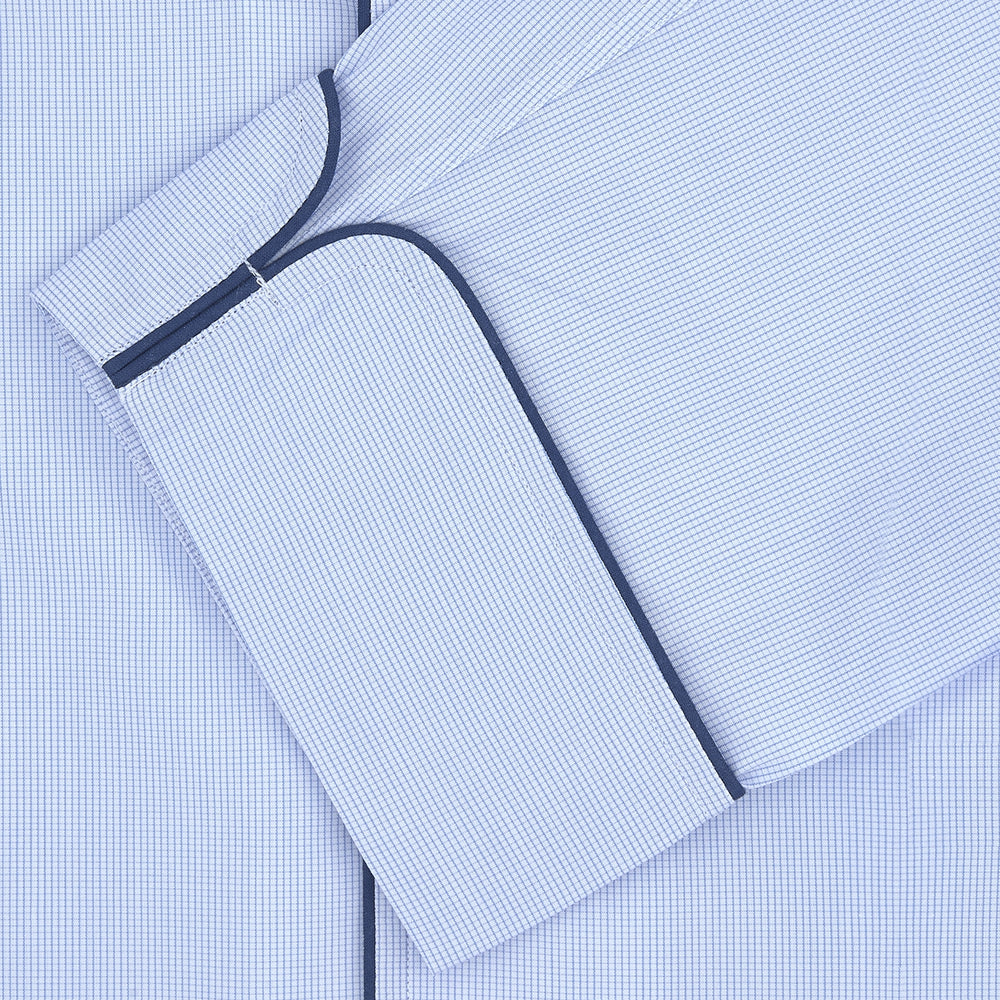 The Turnbull & Asser Light Blue Fine Check Piped Cotton Pyjama Set, crafted from luxurious Egyptian cotton, features a folded top with white buttons, dark piping on the collar, and a matching fabric belt on a plain white background.