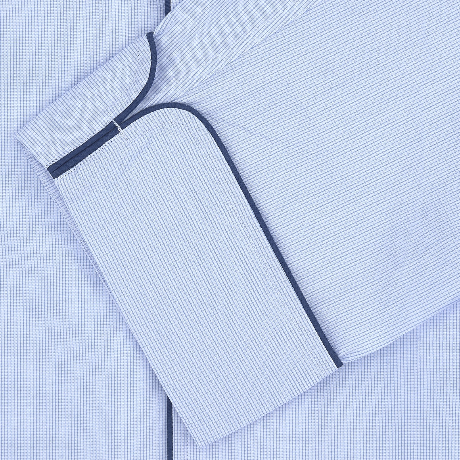 View 2 of product The Turnbull & Asser Light Blue Fine Check Piped Cotton Pyjama Set, crafted from luxurious Egyptian cotton, features a folded top with white buttons, dark piping on the collar, and a matching fabric belt on a plain white background.