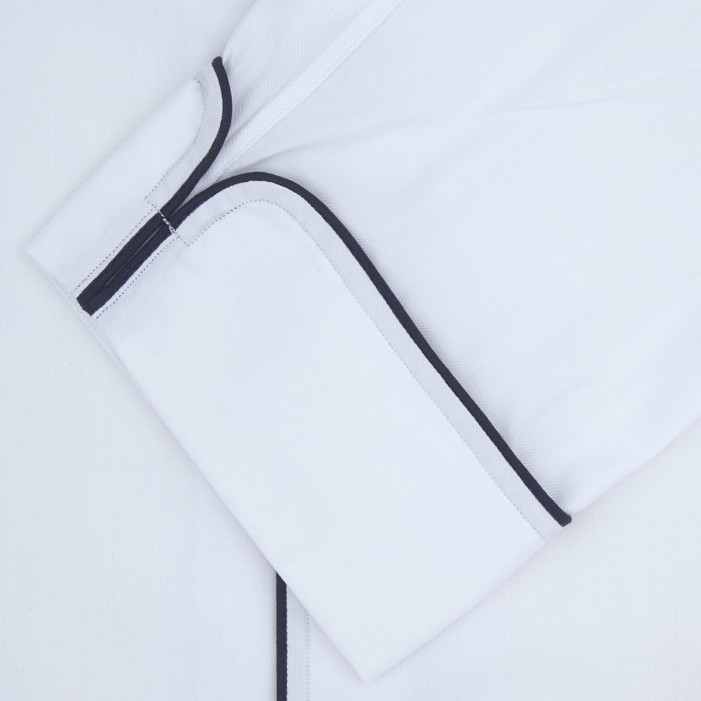 The Turnbull & Asser White Herringbone Piped Superfine Cotton Pyjama Set features a long-sleeve button-up top and drawstring pants with black piping, all crafted from superfine cotton and shown against a plain white background.