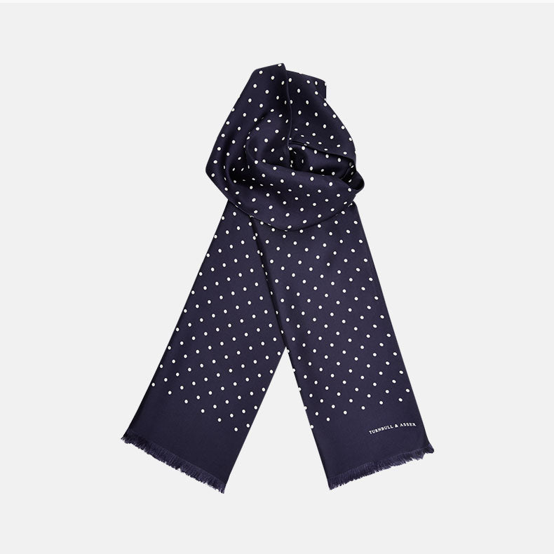 View 1 of product The Navy and White Spotted Silk Scarf by Turnbull & Asser features a hand-printed polka dot design and fringed edges, neatly folded and displayed on a plain white background.