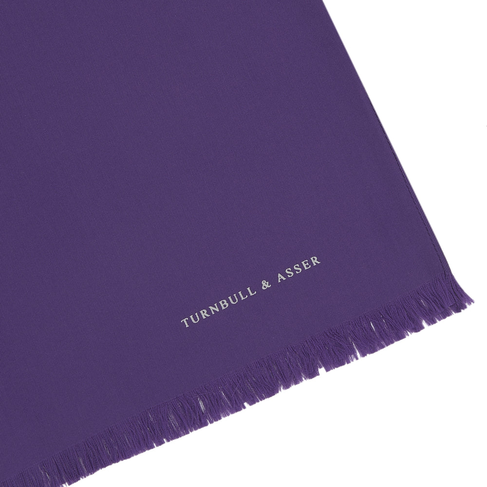 A long, elegant Plain Purple Silk Scarf by Turnbull & Asser, crafted from silk with fringed ends and neatly folded, makes a stylish accessory for any wardrobe.
