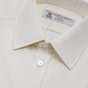 View 5 of product The Turnbull & Asser Cream Herringbone Superfine Cotton Shirt features a T&A collar, double cuffs, and a subtle pattern. It is neatly folded with white buttons and displayed on a plain white background.