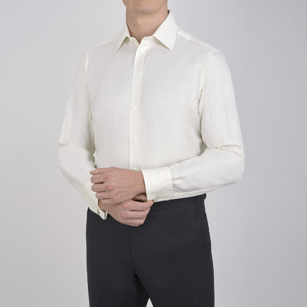 The Turnbull & Asser Cream Herringbone Superfine Cotton Shirt features a T&A collar, double cuffs, and a subtle pattern. It is neatly folded with white buttons and displayed on a plain white background.