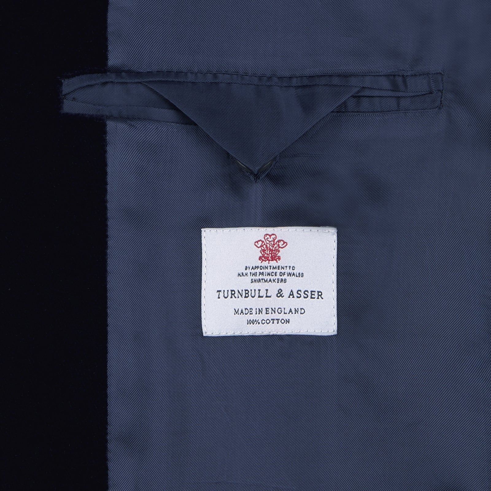 View 2 of product Turnbull & Asser's MSMJ004-ZCS002 "Fergus" velvet smoking jacket in navy features a shawl collar, single decorative knot closure, and two front pockets, shown against a white background.