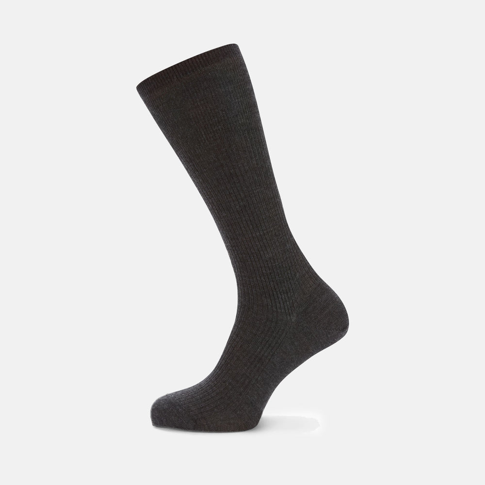 A single Charcoal Mid-Length Merino Wool Sock by Turnbull & Asser stands upright on a light gray background, its dark ribbed fabric and angled foot showcased.