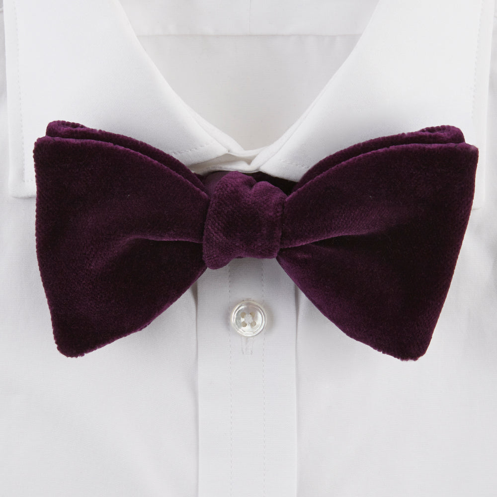 The Turnbull & Asser Purple Velvet Bow Tie is showcased on a plain white background, offering an elegant accessory to elevate any formal outfit with sophistication.
