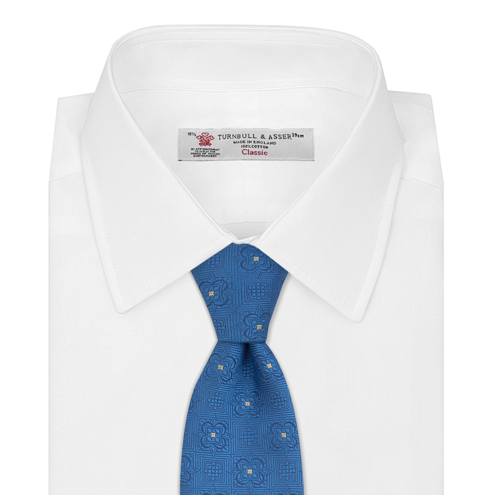 The Turnbull & Asser Blue Flower Mosaic Silk Tie features a blue silk fabric with a detailed geometric and floral design, accented in lighter blue and white, displayed on a white background.