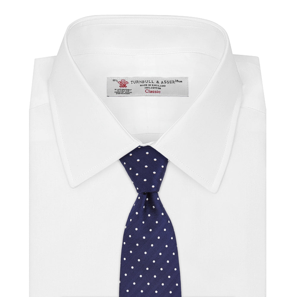 The Turnbull & Asser Slim Navy & White Spot Herringbone Silk Tie features a subtle texture and white polka dots, making it a refined men's accessory. Shown rolled-up on a plain white background.