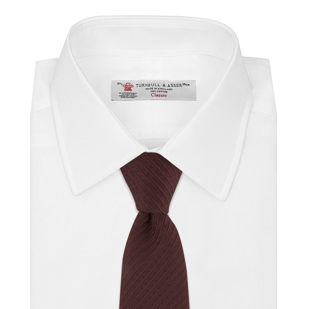 The Turnbull & Asser Burgundy Ottoman Silk Tie features a heavyweight ribbed silk with a subtle diagonal wave pattern, shown rolled up on a plain white background.